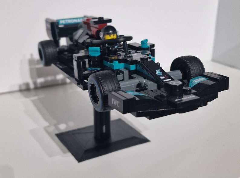 May include: A black and teal Lego Formula 1 race car with the number 6 on the side. The car is on a black stand and has the words "PETRONAS" and "IWC" printed on it.