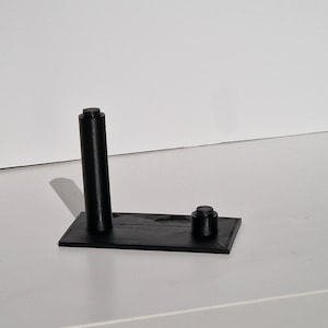 Op de afbeelding: Een zwarte 3D-geprinte standaard met een hoge, cilindrische paal en een kleinere, ronde basis. De standaard is ontworpen om een klein object te houden, zoals een telefoon of een pen.
