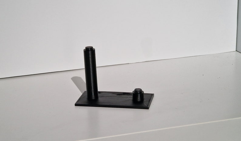 Op de afbeelding: Een zwarte 3D-geprinte standaard met een hoge, cilindrische paal en een kleinere, ronde basis. De standaard is ontworpen om een klein object te houden, zoals een telefoon of een pen.