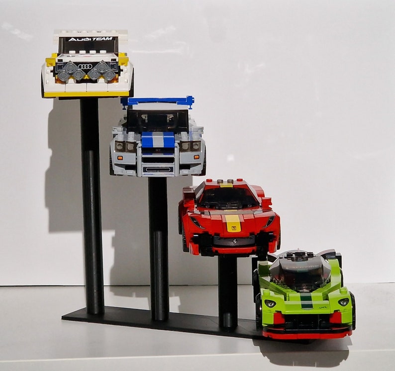 K&ouml;nnte beinhalten: Ein wei&szlig;er, blauer, roter und gr&uuml;ner Lego-Auto-Pr&auml;sentationsst&auml;nder mit vier Autos. Der St&auml;nder hat drei schwarze Metallstangen. Die Autos sind ein wei&szlig;er Audi mit dem Text "Audi Team" auf der Vorderseite, ein blau-wei&szlig;es Auto, ein rotes Auto und ein gr&uuml;nes Auto.