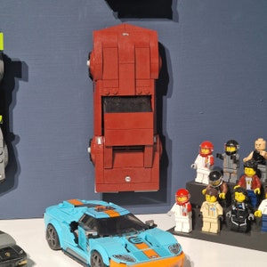 Puede incluir: Un modelo de coche Lego rojo con un parabrisas negro y un modelo de coche Lego azul con un parabrisas negro. Los coches est&aacute;n sobre un fondo azul. Tambi&eacute;n hay figuras de Lego en el fondo.