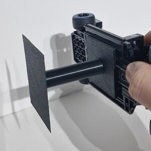 May include: A black Lego car model with blue wheels is mounted on a black stand with a square base. The stand is made of a 3D printed material.