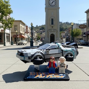 May include: A Lego DeLorean time machine model from the movie Back to the Future, with two Lego figures. The car is gray with blue accents and hovers above a black base with the movie title. The background shows a town square.