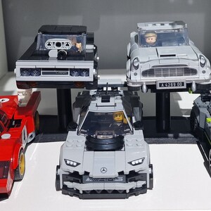 May include: Five miniature Lego cars on display. A red race car, a gray sports car, a black car, a silver car, and a gray and green car.