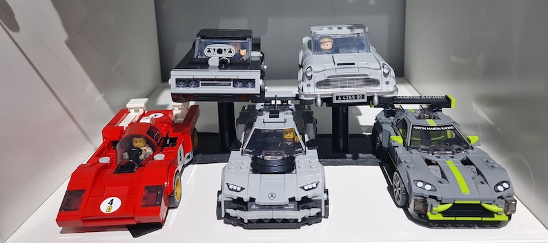 May include: Five miniature Lego cars on display. A red race car, a gray sports car, a black car, a silver car, and a gray and green car.