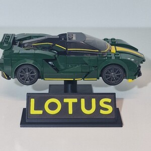 May include: A green and yellow LEGO Lotus sports car model on a black display stand with the word "LOTUS" in yellow letters.
