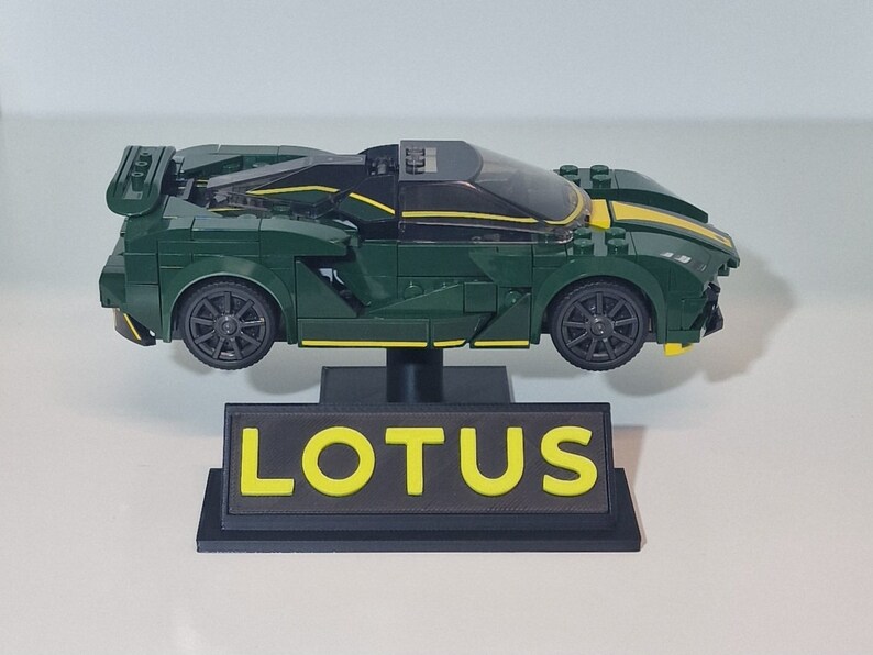 May include: A green and yellow LEGO Lotus sports car model on a black display stand with the word "LOTUS" in yellow letters.