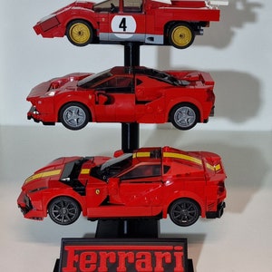 Puede incluir: Tres coches de carreras Lego Ferrari rojos en un soporte negro con la palabra "Ferrari" impresa en la parte delantera. Los coches est&aacute;n apilados uno encima del otro, con el coche superior con el n&uacute;mero "4" en el lateral.