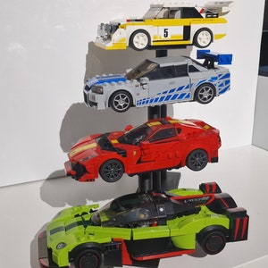 K&ouml;nnte beinhalten: Ein mehrstufiger Displayst&auml;nder mit vier Spielzeugautos. Das oberste Auto ist wei&szlig; mit gelben Akzenten und der Nummer "5" an der Seite. Das zweite Auto ist grau mit blauen und wei&szlig;en Streifen. Das dritte Auto ist rot mit schwarzen Akzenten. Das unterste Auto ist gr&uuml;n mit schwarzen und roten Akzenten.