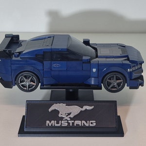 May include: A blue Lego model of a Ford Mustang with a black spoiler and a silver Mustang logo on a black display stand.
