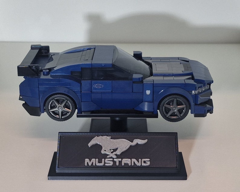 May include: A blue Lego model of a Ford Mustang with a black spoiler and a silver Mustang logo on a black display stand.