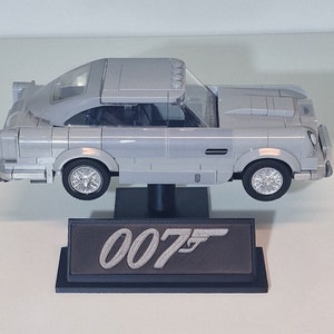 May include: A silver Lego model of the iconic Aston Martin DB5 from the James Bond films, displayed on a black stand with the 007 logo.