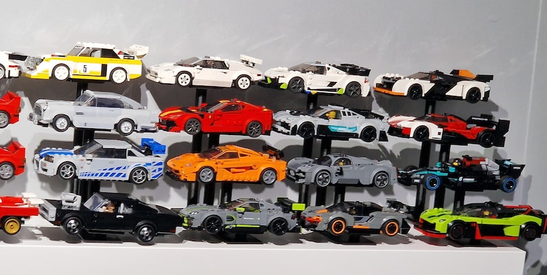 K&ouml;nnte beinhalten: Eine Sammlung von 15 Miniatur-Spielzeugautos, die auf einem schwarzen St&auml;nder ausgestellt sind. Die Autos sind eine Mischung aus Rot, Wei&szlig;, Schwarz, Blau, Gr&uuml;n, Orange und Grau. Die Autos sind alle von verschiedenen Marken und Modellen, darunter ein Rennwagen, ein Sportwagen und ein LKW.