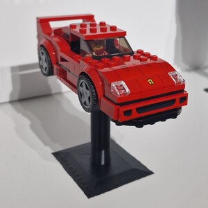 May include: A red Lego Ferrari F40 model car with a black base and a Lego figure in the driver's seat.