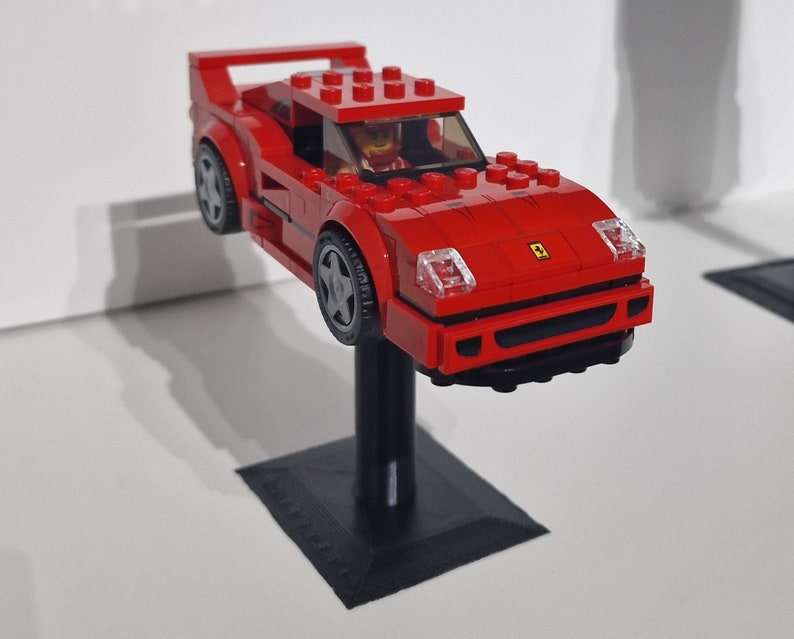 May include: A red Lego Ferrari F40 model car with a black base and a Lego figure in the driver's seat.