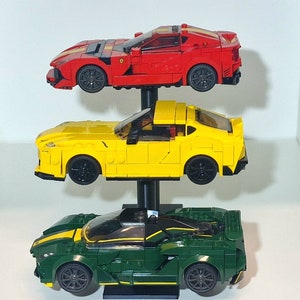 May include: Three toy race cars on a display stand. The top car is red, the middle car is yellow, and the bottom car is green.