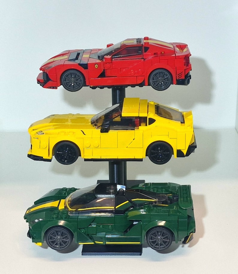 May include: Three toy race cars on a display stand. The top car is red, the middle car is yellow, and the bottom car is green.