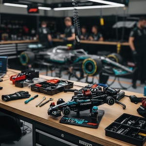 May include: A detailed shot of a workshop bench with a black and teal Lego Formula 1 race car model. The model sits on a black base with the text "W12 16". Various tools, gloves, and a laptop are also on the wooden surface.