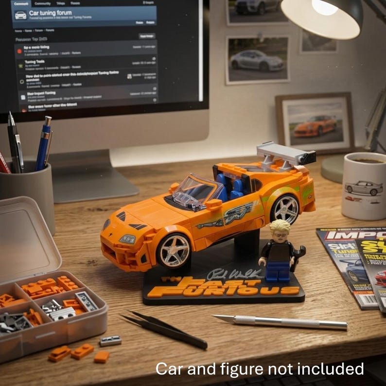 Pu&ograve; includere: Un modellino di auto in plastica arancione con alettone posteriore e ruote argentate, montato su una base nera con la scritta Fast & Furious e una firma. Una piccola minifigure bionda &egrave; in piedi accanto all'auto sulla base, tenendo una chiave inglese.