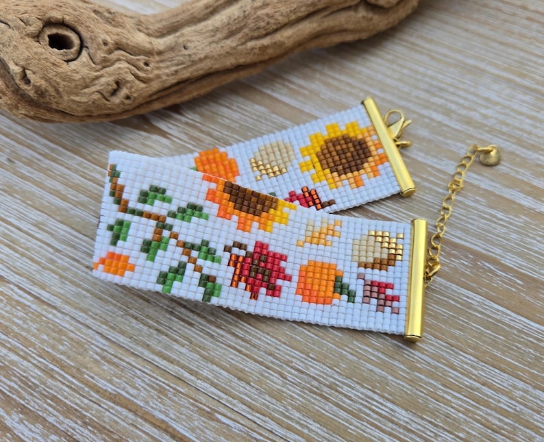 Peut inclure: Deux bracelets perl&eacute;s blancs avec fermoirs et cha&icirc;ne dor&eacute;s. Les bracelets pr&eacute;sentent un motif sur le th&egrave;me de l'automne avec des tournesols, des citrouilles et des feuilles d'automne en orange, marron et rouge. Les bracelets sont sur une surface en bois.