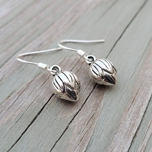 May include: A pair of silver dangle earrings with a detailed, textured, leaf-shaped design.