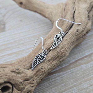 May include: A pair of silver dangle earrings with a delicate wing design. The wings are detailed and have a slightly textured finish.