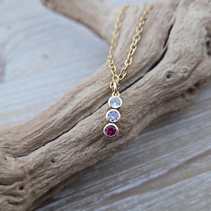 May include: A gold chain necklace with a pendant featuring three small round stones. The stones are arranged vertically, with a pink stone at the bottom, a white stone in the middle, and a clear stone at the top.