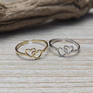 May include: Two dainty rings with a double heart design. One ring is gold and the other is silver.