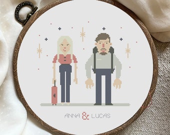 Peut inclure: Un cercle de broderie en point de croix avec un fond blanc représentant deux personnages pixélisés, une femme aux cheveux blonds et un homme aux cheveux bruns, debout côte à côte. Les personnages tiennent des valises et de petites étoiles sont éparpillées autour d'eux. Le texte "ANNA & LUCAS" est écrit sous les personnages.
