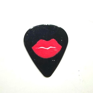May include: Black guitar plectrum with a red lip design. The glossy plectrum has a teardrop shape and a white background. The red lips are centered on the pick.