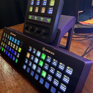 May include: Two black Stream Deck controllers with a variety of buttons and labels. The top controller has a small screen displaying "Sep 25 my" and "77". The bottom controller has labels like "Guest 1 Content", "Guest 2 Content", and "Camera".