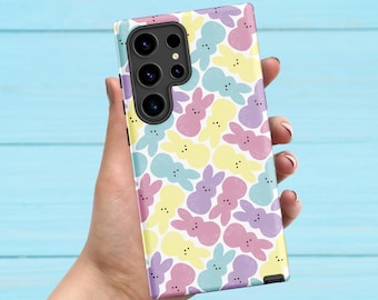 May include: A phone case featuring a repeating pattern of pastel-colored bunny shapes in pink, yellow, blue, and purple. The case has a camera cutout and is held against a light blue background.
