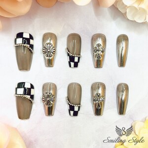 May include: Set of ten false nails with a silver cross design and a black and white checkered pattern. The nails are arranged in two rows of five.