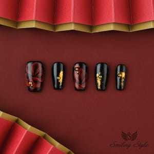 May include: Five black press-on nails with red and gold floral designs. The nails are arranged in a row on a red background.