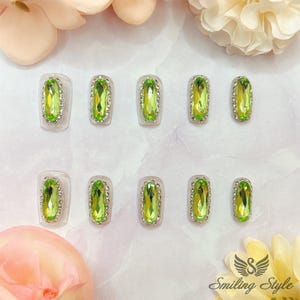 May include: Ten green oval-shaped rhinestones on a white background. The rhinestones are set in silver settings and are arranged in two rows of five.