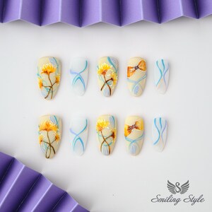 May include: Ten false fingernails with different designs. Some nails have yellow flowers with blue stems and leaves, others have blue and white swirls, and two have brown bows.