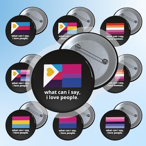 Op de afbeelding: Een verzameling zwarte buttons met verschillende LGBTQ+ pride vlaggen en de tekst "what can I say, I love people." De buttons tonen ontwerpen die verschillende identiteiten vertegenwoordigen, tegen een blauwe achtergrond.