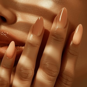 May include: Close-up of a hand with long, oval-shaped nails painted in a nude ombre design. A silver ring is on the ring finger. The skin has a warm, golden tone, and the background features striped shadows.