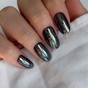 May include: Close-up of a hand with oval-shaped nails painted with a dark, iridescent, metallic polish.
