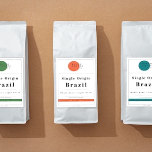 Puede incluir: Tres bolsas blancas de café de grano entero tostado ligero etiquetadas como "Single Origin Brazil" de Bloom Coffee Co. Las bolsas tienen un logotipo circular verde, naranja y azul con el nombre de la empresa.