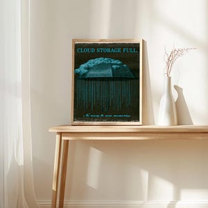 Small framed poster on a slim table with white ceramic vases. The image shows the cyan-coded umbrella and cloud on a dark textured background with distressed light paper border.