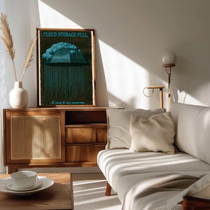 Tall framed print on a console beside a vase and vintage camera. The neon-cyan umbrella made of 1s and 0s and the headline 'CLOUD STORAGE FULL.' are clearly visible against the grained dark background.