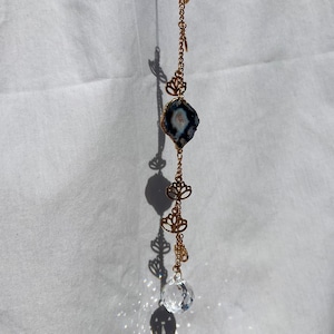 May include: A gold-toned crystal suncatcher with a large agate slice and multiple lotus flower charms. The suncatcher hangs from a clear string.