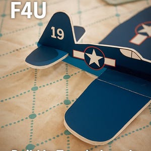 May include: A blue paper airplane with white details and a star emblem. The number 19 is on the tail. The image includes the text "ChuckGlider F4U" and "Build It. Toss It. Love It."