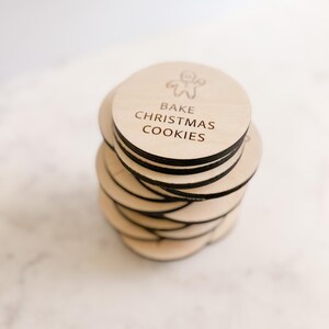 Puede incluir: Una pila de adornos redondos de madera con el texto "Bake Christmas Cookies" y una ilustraci&oacute;n de un hombre de jengibre.