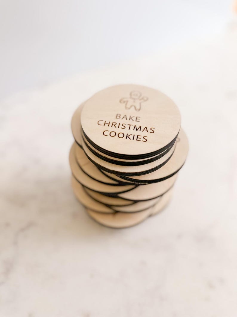 Puede incluir: Una pila de adornos redondos de madera con el texto "Bake Christmas Cookies" y una ilustraci&oacute;n de un hombre de jengibre.