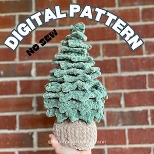 May include: A green crocheted Christmas tree with a brown crocheted base. The tree is made with a fuzzy yarn and has a layered, tiered design. The image includes the text "DIGITAL PATTERN NO SEW" and "@handmadeby_the_ann".