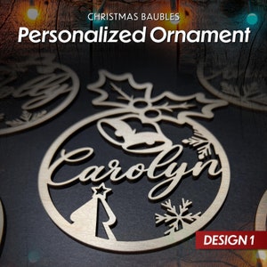 May include: A wooden Christmas bauble with a holly design, a bell, a snowflake, and a Christmas tree. The bauble is personalised with the name "Carolyn" and the text "DESIGN 1".