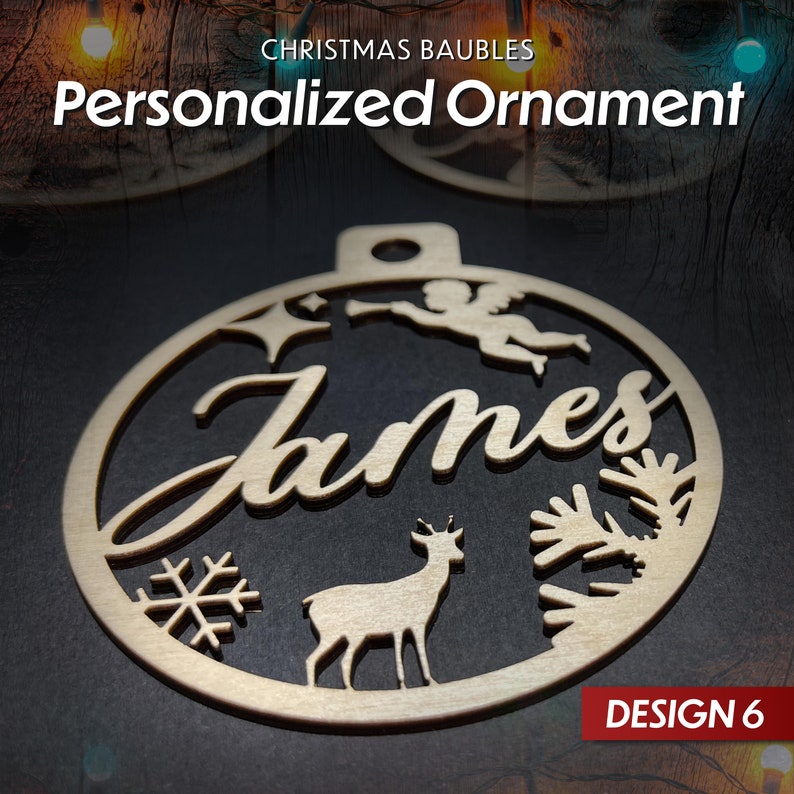 May include: A wooden Christmas bauble with a cut-out design featuring a deer, a snowflake, a star, an angel, and the name "James". The bauble is round and has a hole at the top for hanging. The text "DESIGN 6" is visible in the bottom right corner.