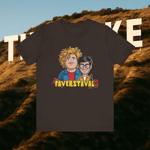 Könnte beinhalten: Dunkelbraunes T-Shirt mit einer Cartoon-Illustration von zwei Männern und dem Text "FAVERSTAVAL". Der Hintergrund zeigt das Hollywood-Zeichen auf einem Hügel.